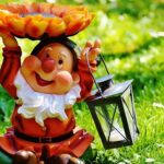 Cheerful German garden gnome holding a sunflower and lantern on a sunny lawn