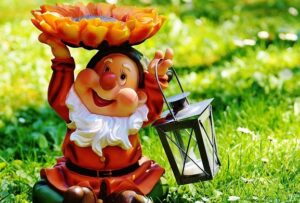 Cheerful German garden gnome holding a sunflower and lantern on a sunny lawn
