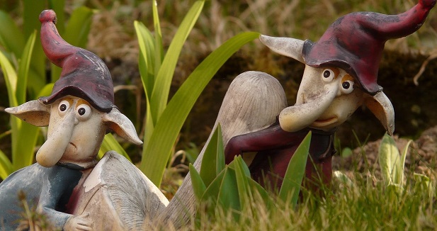 Playful garden gnomes in whimsical design Two whimsical garden gnomes with long noses and red hats sitting among grass and plants